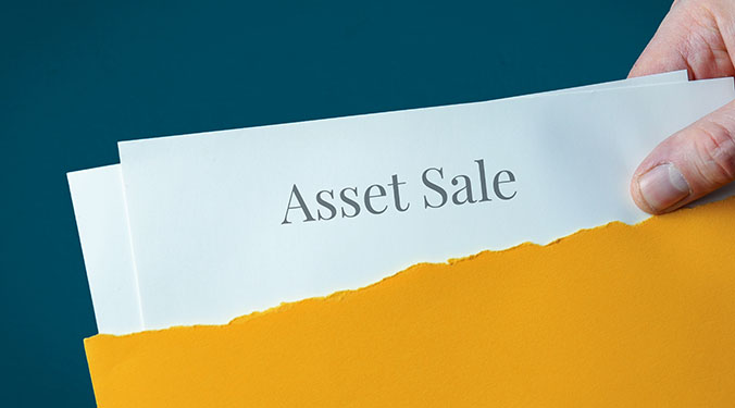 The words 'asset sale' printed on white piece of paper inside yellow folder.