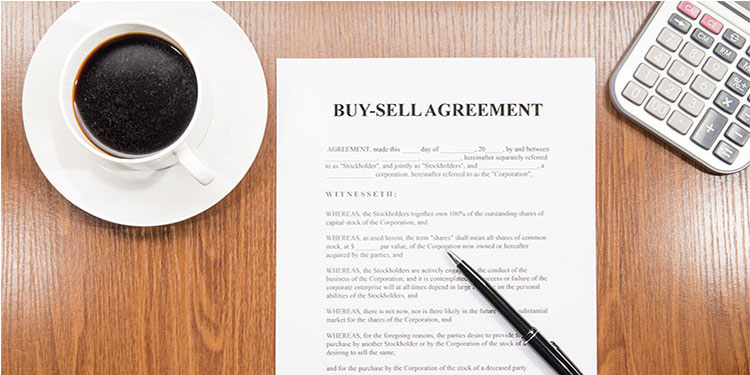 A buy-sell agreement contract on desk with coffee cup and calculator.