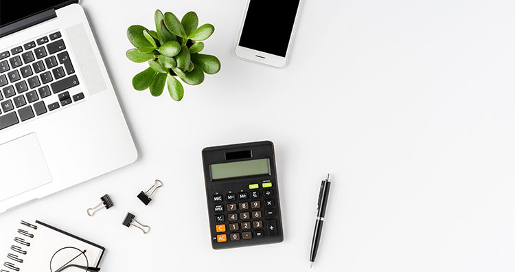 Calculator on desk with laptop, phone, plant, and assorted office supplies.