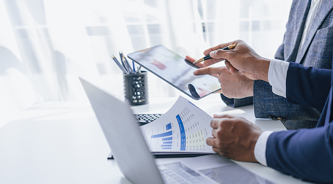 Businessmen at conference table negotiating financing with spreadsheets and tablets. 