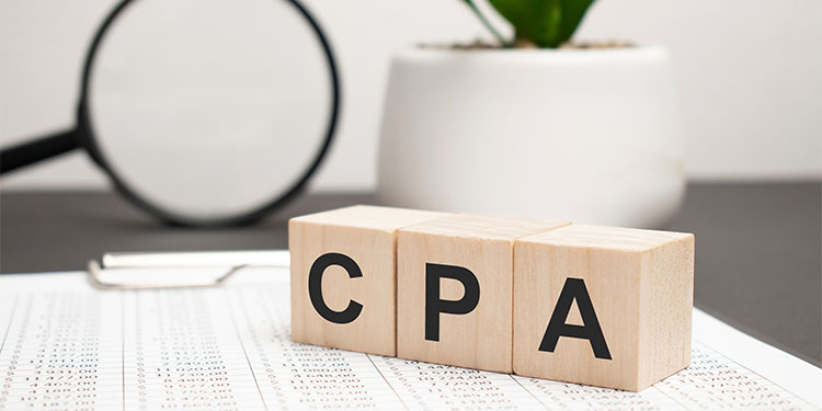 The term "CPA" spelled out on wooden blocks, placed on accounting documents on desk. 
