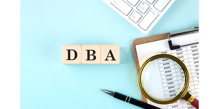 The acronym "DBA" for Doing Business As on Scrabble tiles next to spreadsheets.
