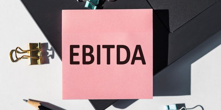 The acronym EBITDA, written on a pink post it note, with assorted office supplies.