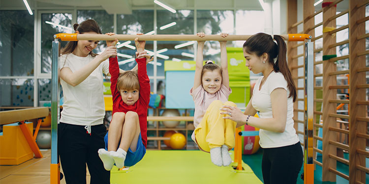 Childrens indoor play center with two kids playing on gym equipment with two instructors guiding.