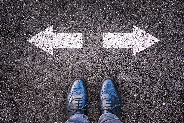 Feet and two arrows painted on an asphalt road, pointing different directions to indicate two choices.