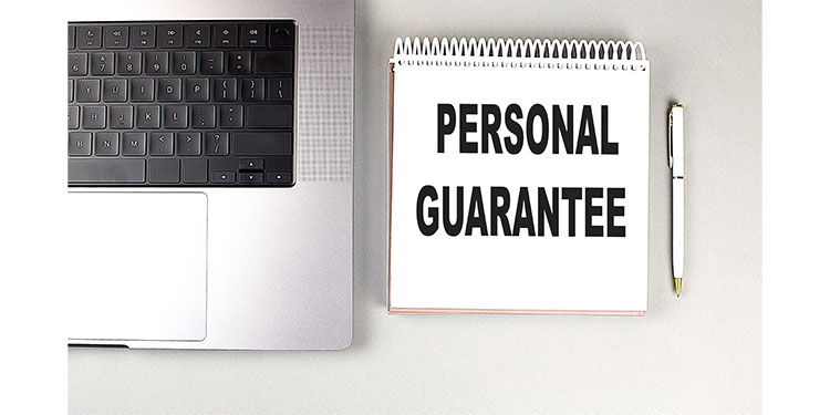 The words "personal guarantee" printed on notebook that is placed on a desk next to a computer.