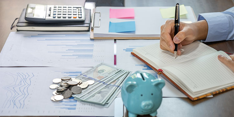 Retirement fund calculations depicted with calculator, notepad, spreadsheets, and piggy bank.