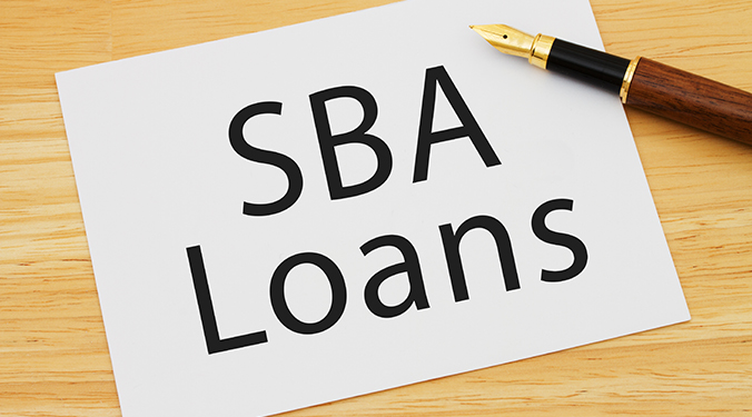 The term "SBA Loan" written on a notepad, placed on desk. 