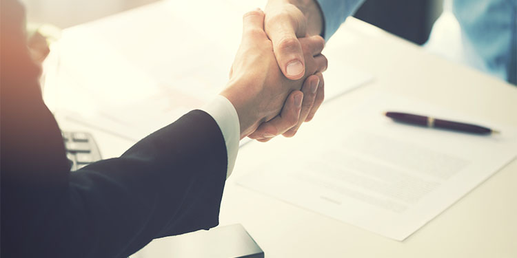 Business partners shaking hands at table with business contracts. 