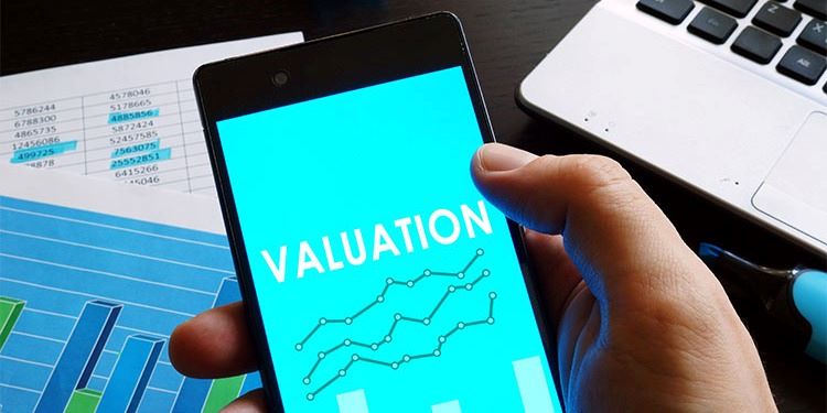 Business valuation image featuring a cell phone with the word 'valuation' with spreadsheets and a computer.