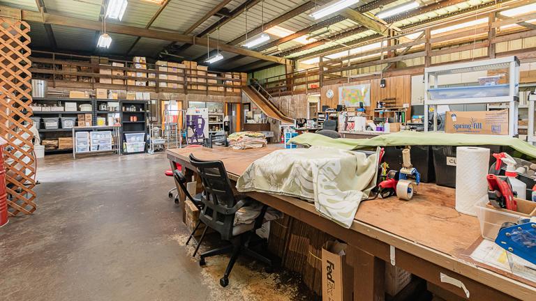 Expansive warehouse with mezzanine storage, central packing tables, and office stations—ample room for fulfillment and shipping growth