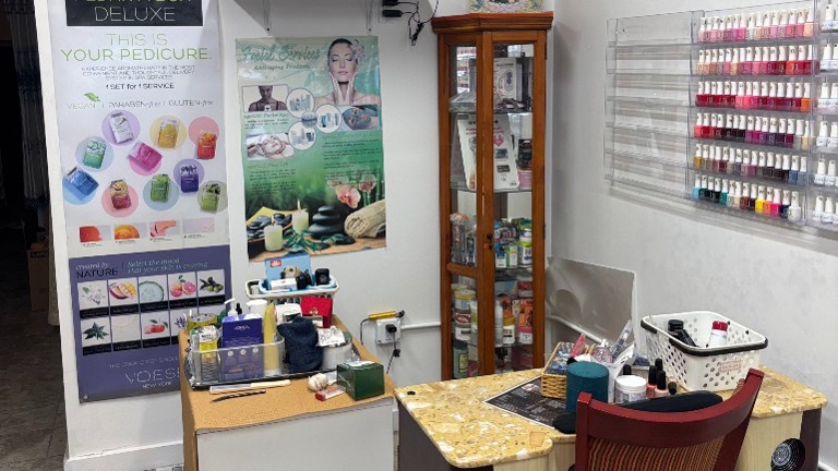Marble-top manicure station with supplies; posters for pedicure and facial services displayed.