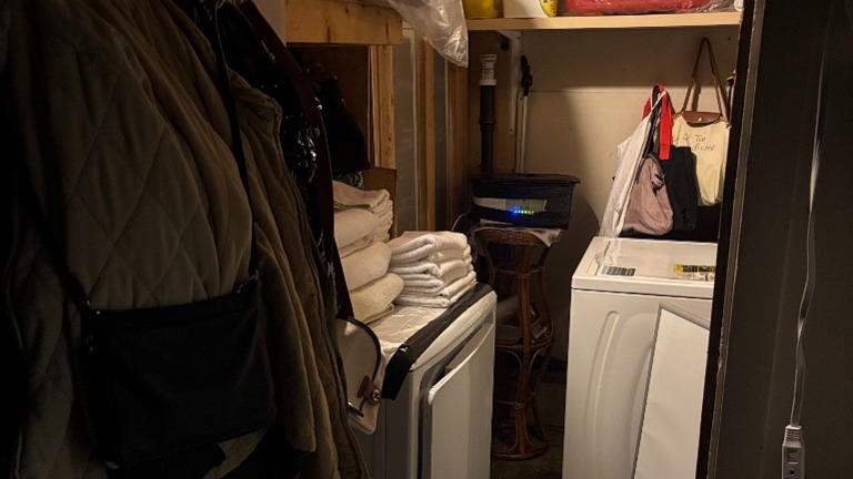 Utility closet with washer, folded towels, shelving, and storage.