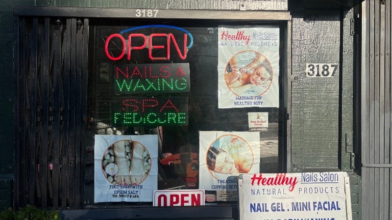 Building exterior with signage for nail salon and spa services; secure entry gate.