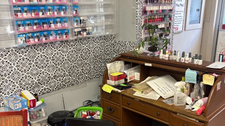 Nail service desk with technician seating; acetone and supplies visible; full wall of polish colors behind.