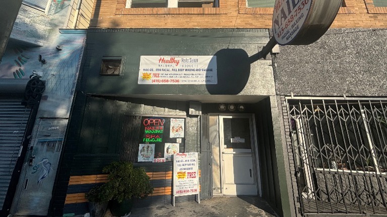 Building exterior with signage for nail salon and spa services; secure entry gate.